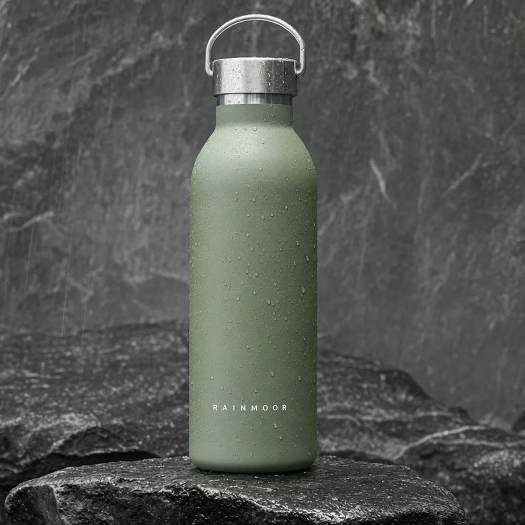AI-generated example product-angle ad for Rainmoor, a fictional drinkware brand: a sage-green insulated bottle on wet slate beaded with rain